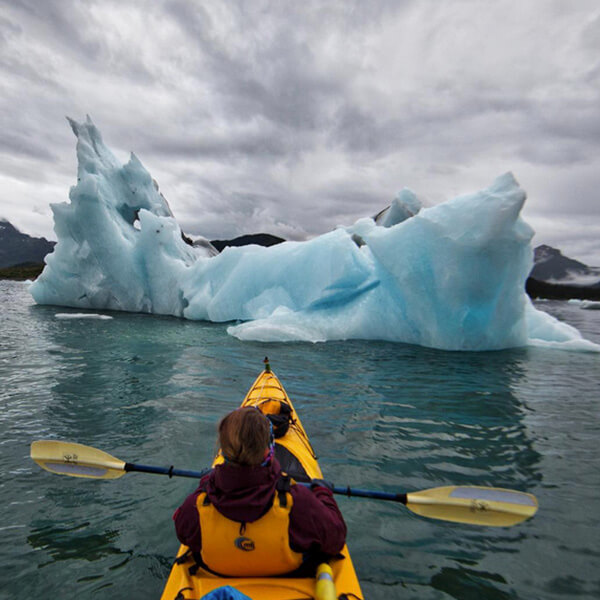 a kayaker in the sea in front of an iceberg