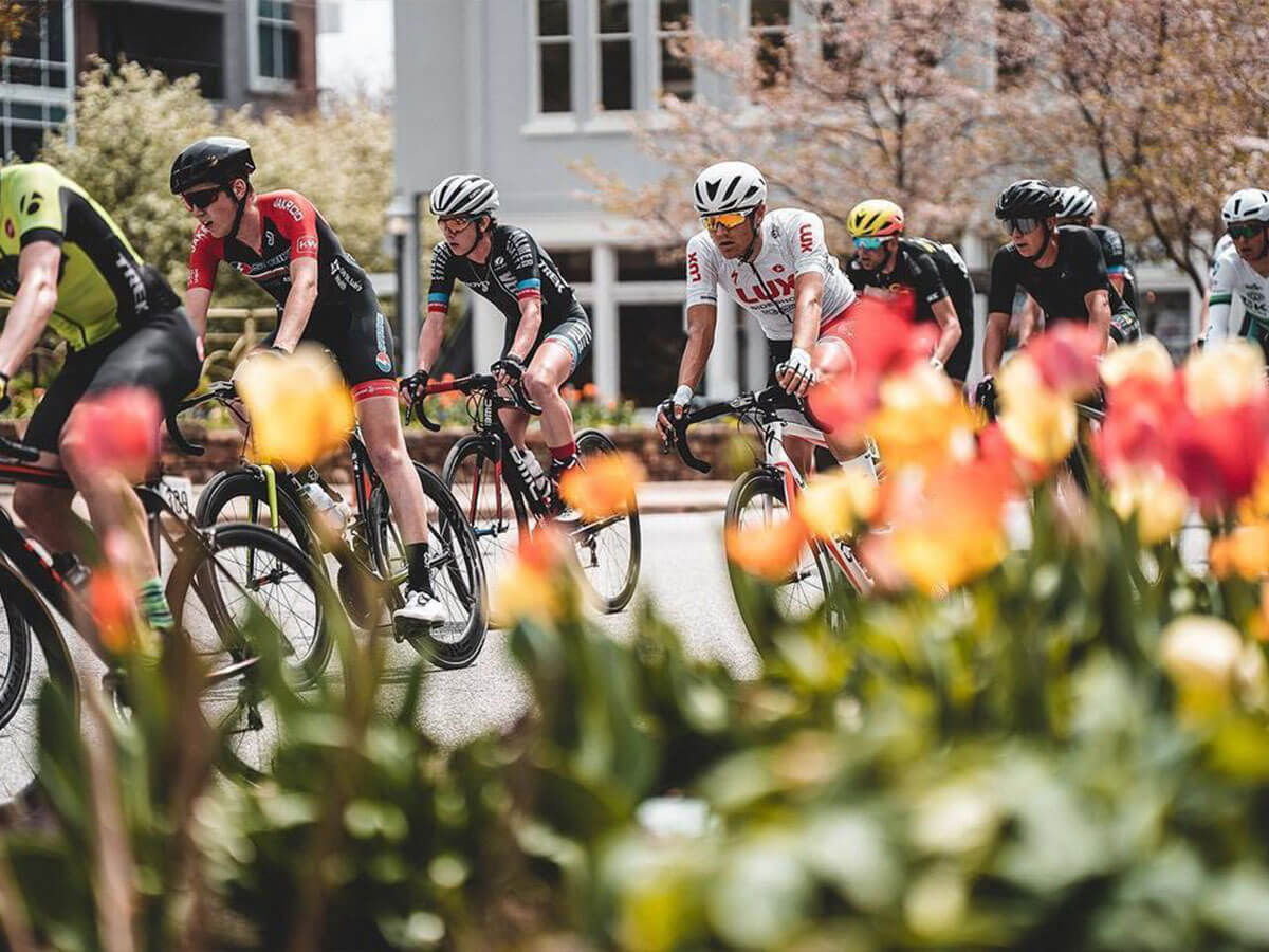 a group of bicyclists passes by some flowers