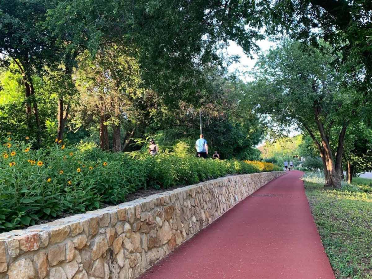 a maroon bike path along the katy trail surrounded by green space and planters