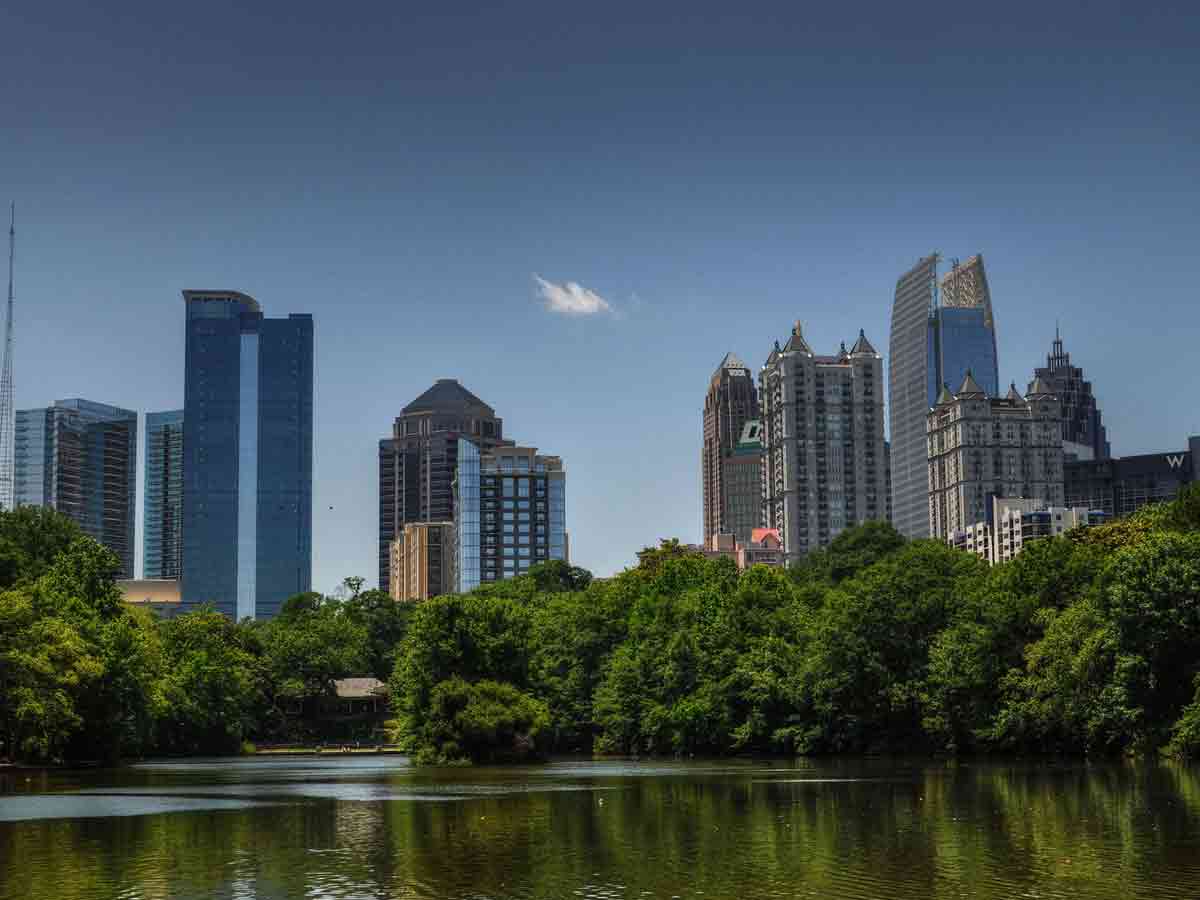 a lake in piedmont park in the foreground and the atlanta skyline in the background behind the park