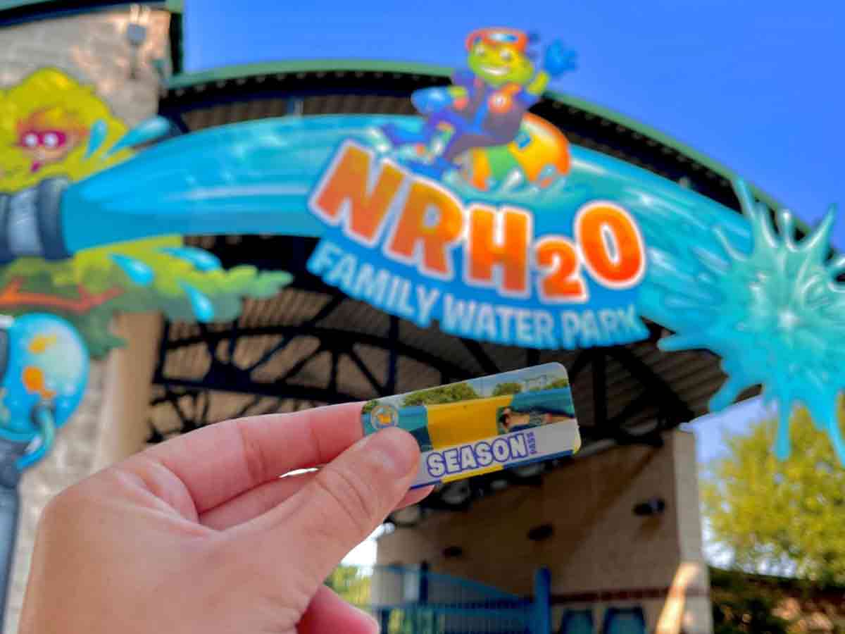 a season pass is held up in front of the entrance sign to NRH2O family water park