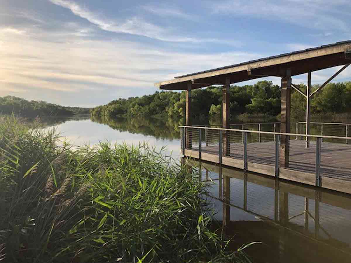 a boardwalk jutting out into the trinity river surround by greenery at the fort worth nature center and refuge