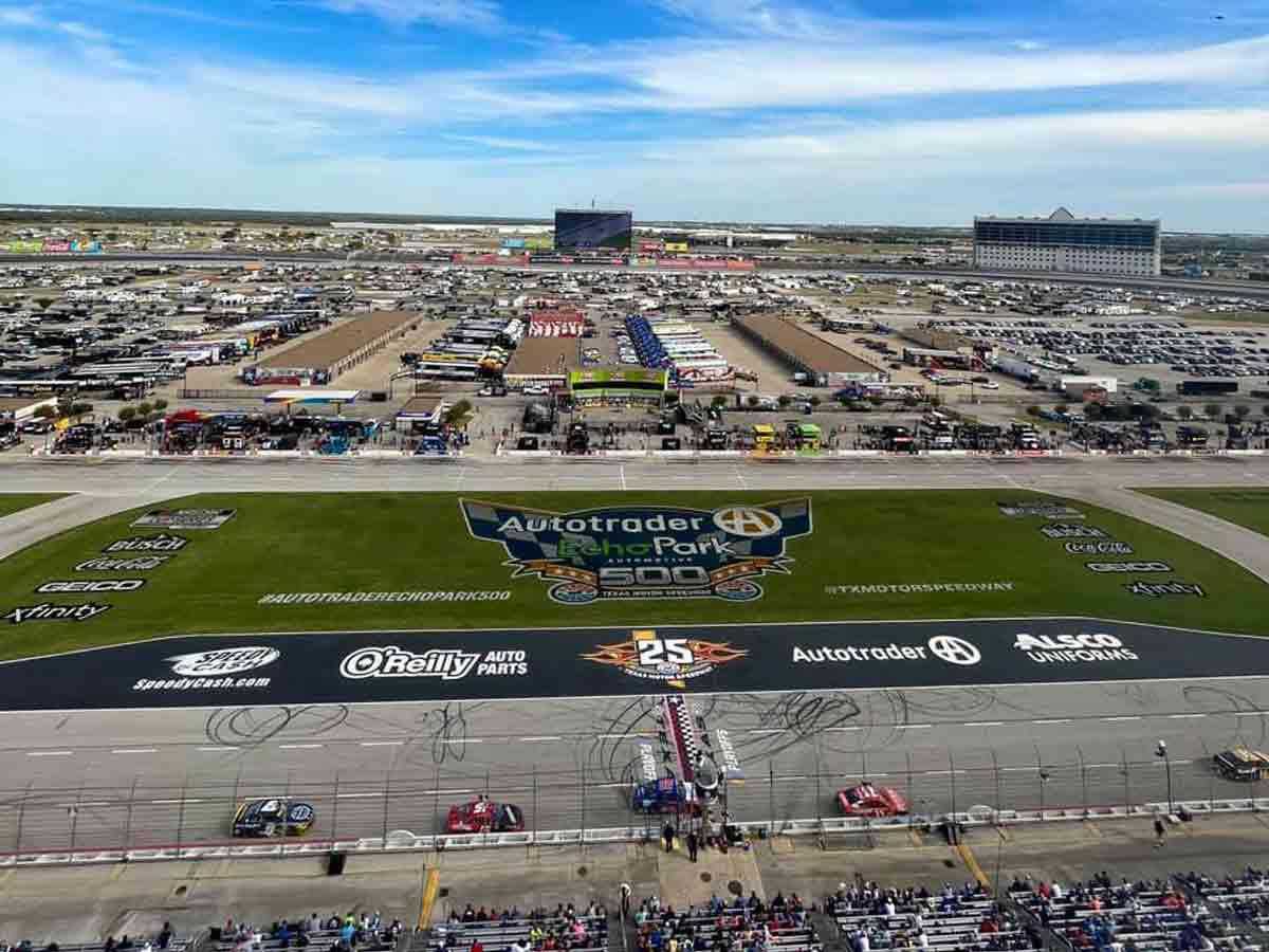 the infield of the texas motor speedway with many vehicles and people watching a NASCAR race