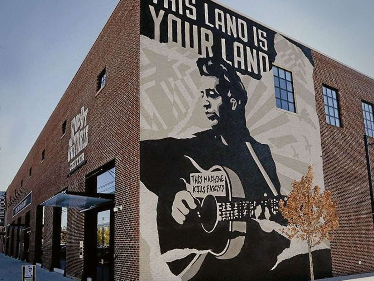 a mural of woody guthrie on the exterior of the woody guthrie museum