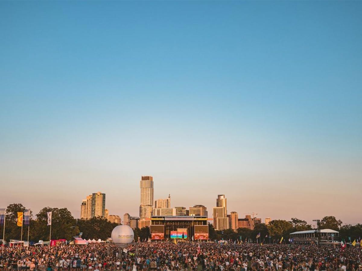 an expansive view of acl fest with the austin skyline of buldings in the background behind festival crowds