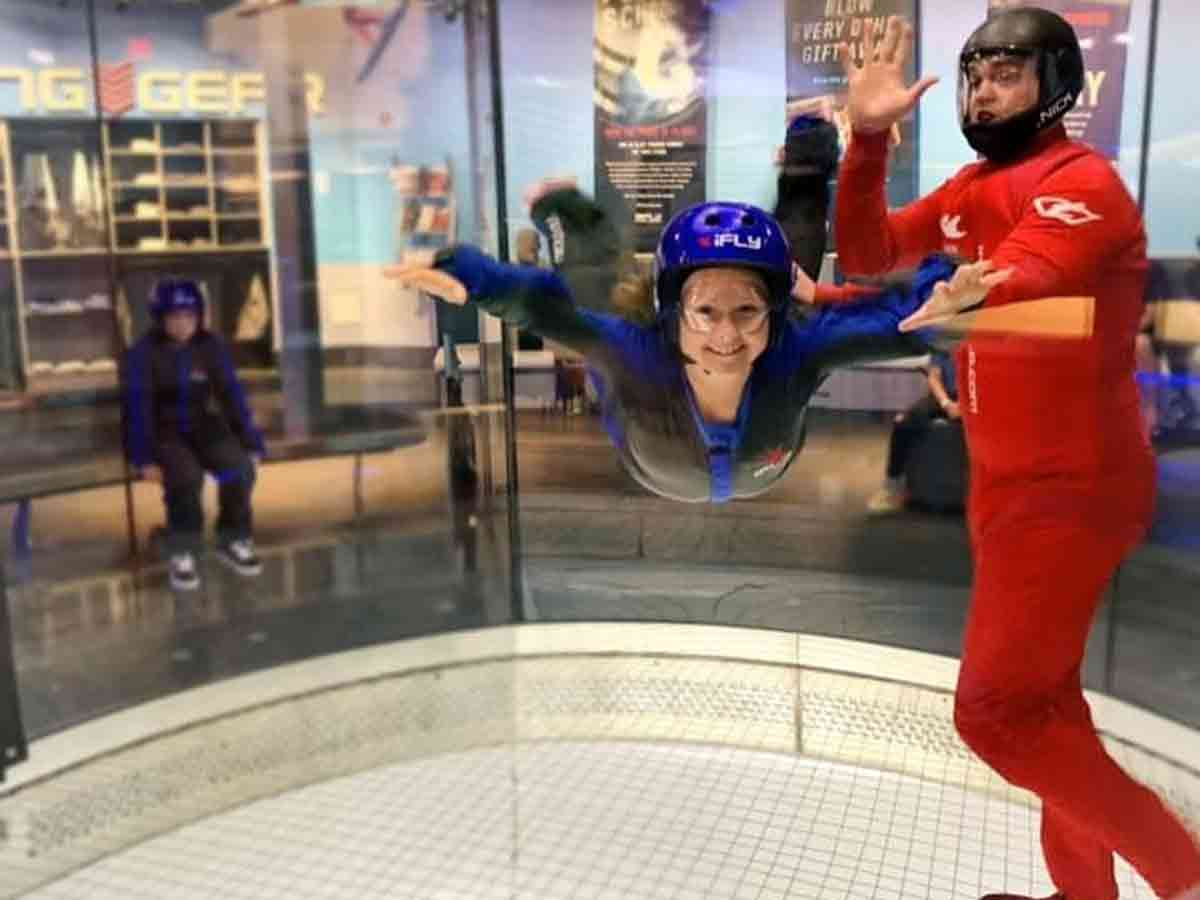 an instructor holds a person hovering over a giant fan in an indoor skydiving center
