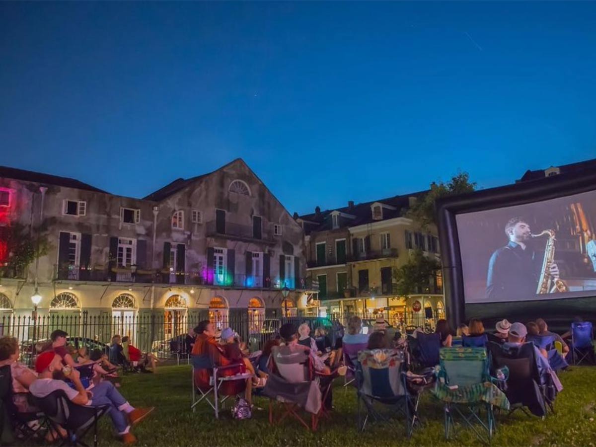 people watching a jazz concert on an outdoor movie screen at night