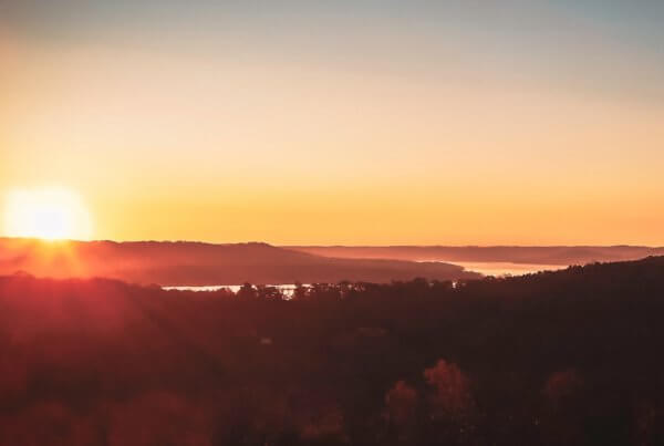 a sun sets behind the mountains surrounding table rock lake in branson missouri