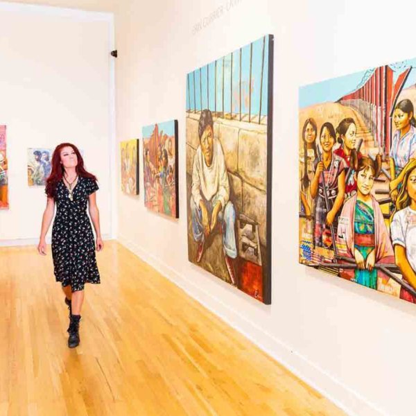 a woman walks through the harwood museum of art gallery looking at paintings on the wall in taos