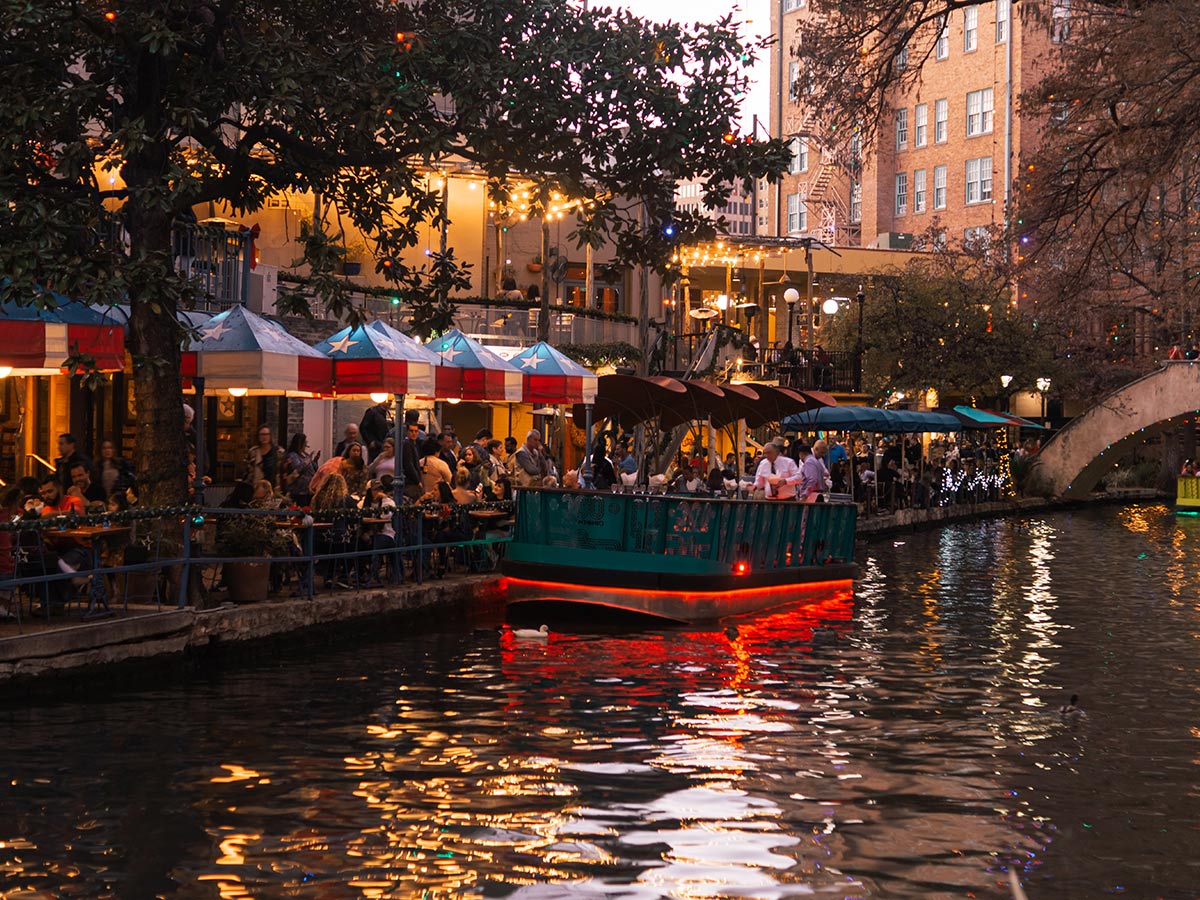 a view down the san antonio river walk at night with lights on stores and boats
