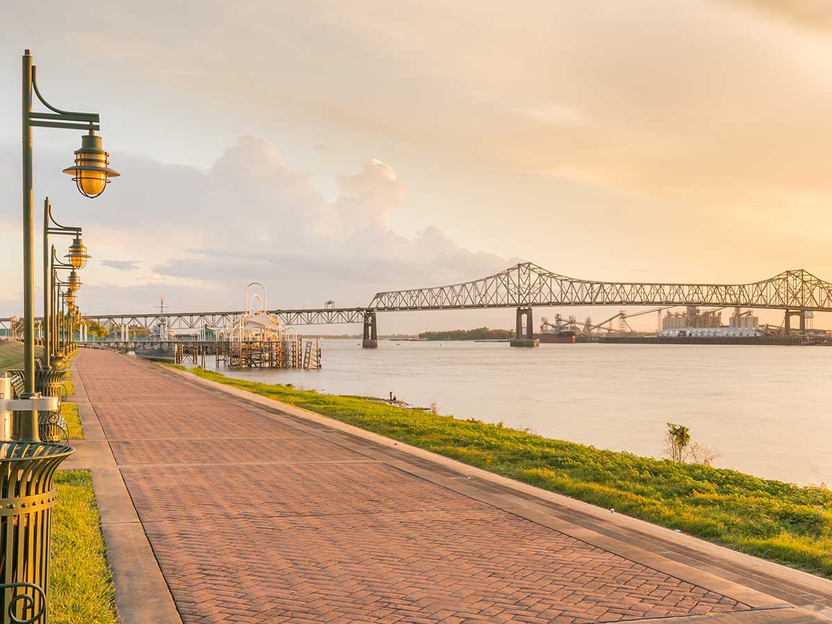 a view of a walking promenade alongside the mississippi river and a bridge crossing the river