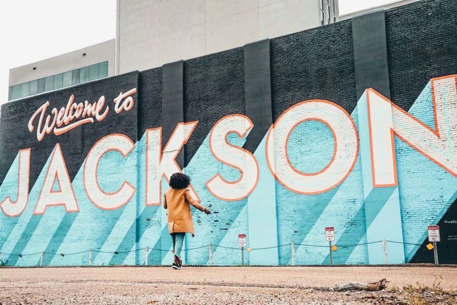 a woman stands in front of a mural that says welcome to jackson mississippi