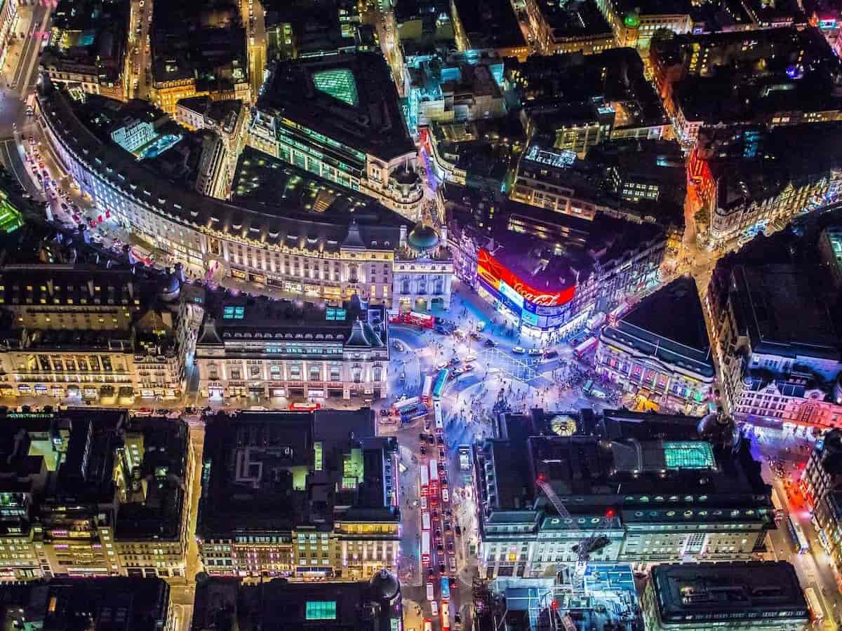 a nighttime aerial view of piccadilly circus among street intersections that glows bright with neon lights
