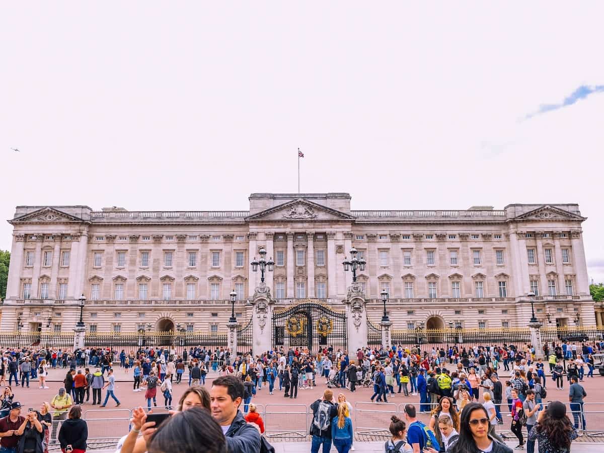 crowds stand in front of the front gates to buckingham palace in london