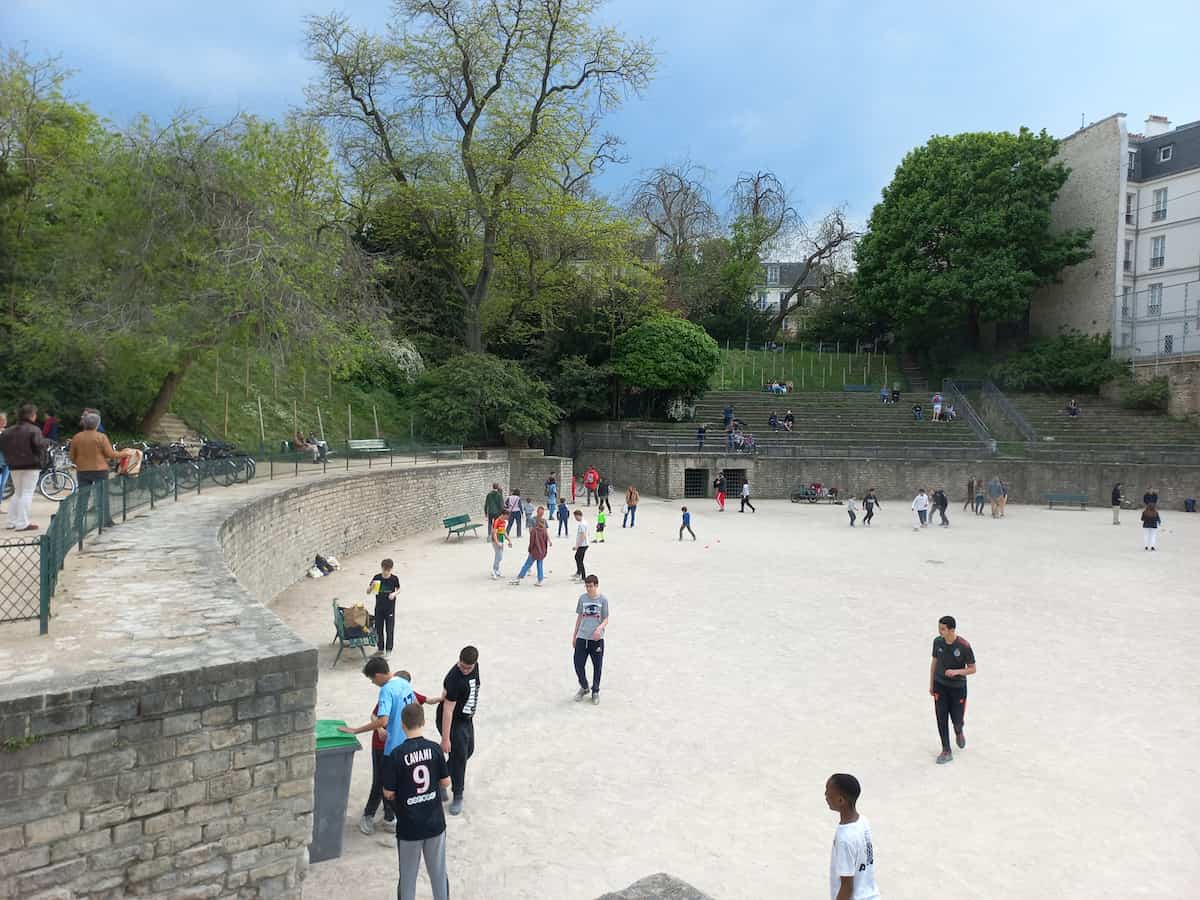 people walk around and play within the Arènes de Lutèce an ancient roman ampitheatre in paris