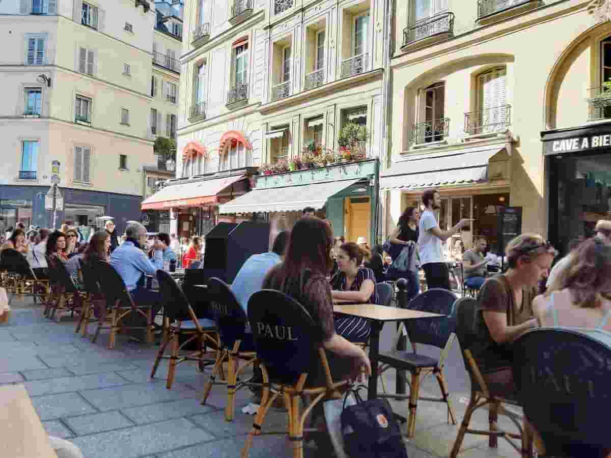 people sit at cafe tables alongside rue de buci a street in paris