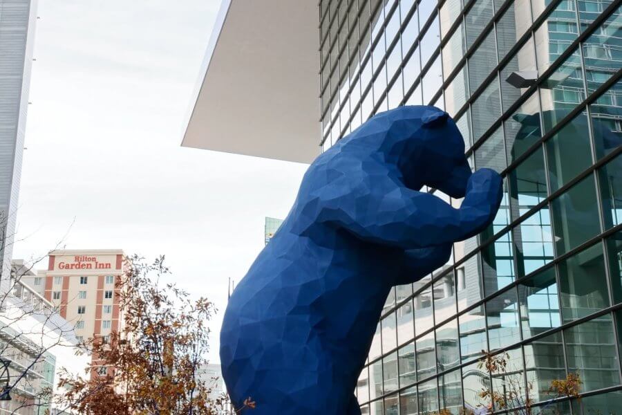a large blue bear sculpture looks into the windows of the colorado convention center in denver