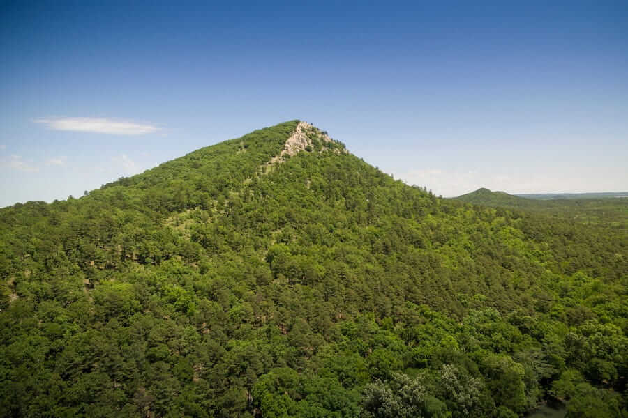 a view of pinnacle mountain in the summer covered in green trees