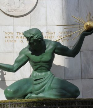 a close up view of the sculpture titled The Spirit of Detroit, a large male figure holding a golden ray in one hand and a small family in the other
