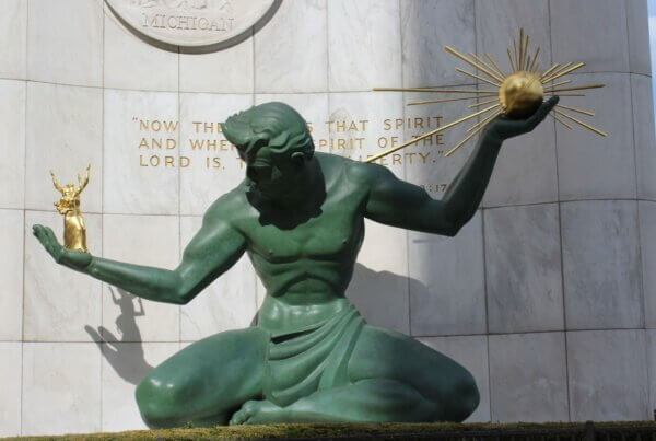 a close up view of the sculpture titled The Spirit of Detroit, a large male figure holding a golden ray in one hand and a small family in the other