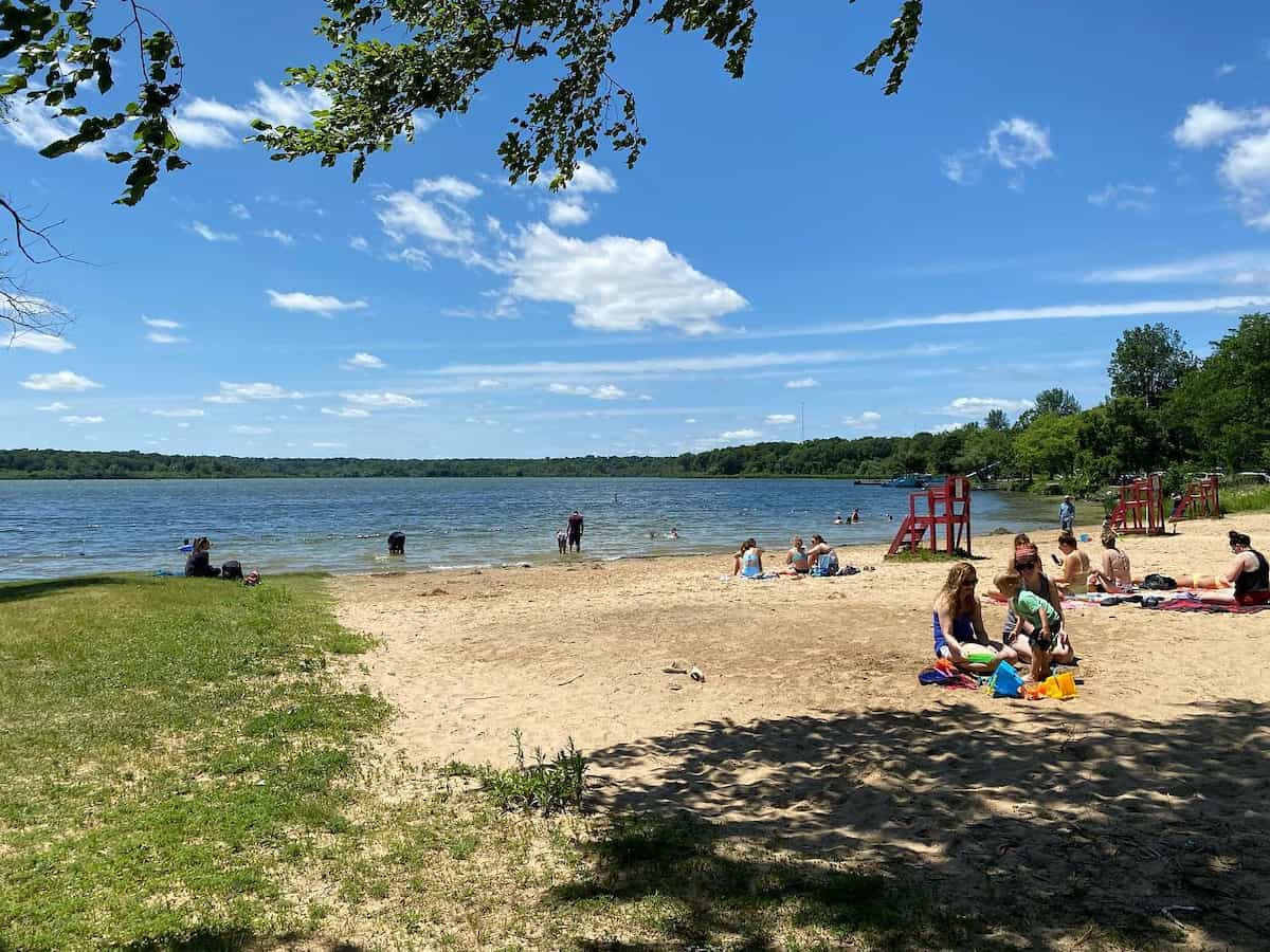 visitors sit in the sand at vilas park beach in madison