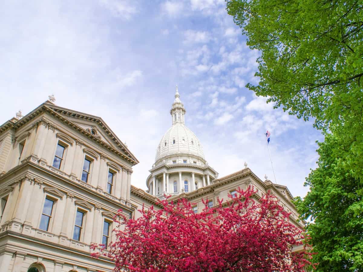 the michigan capitol building in lansing surrounded by green and red trees