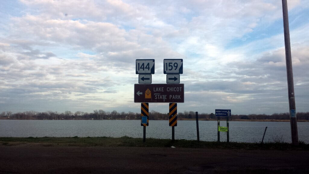 View of a road sign for Lake Chicot with the lake in the background