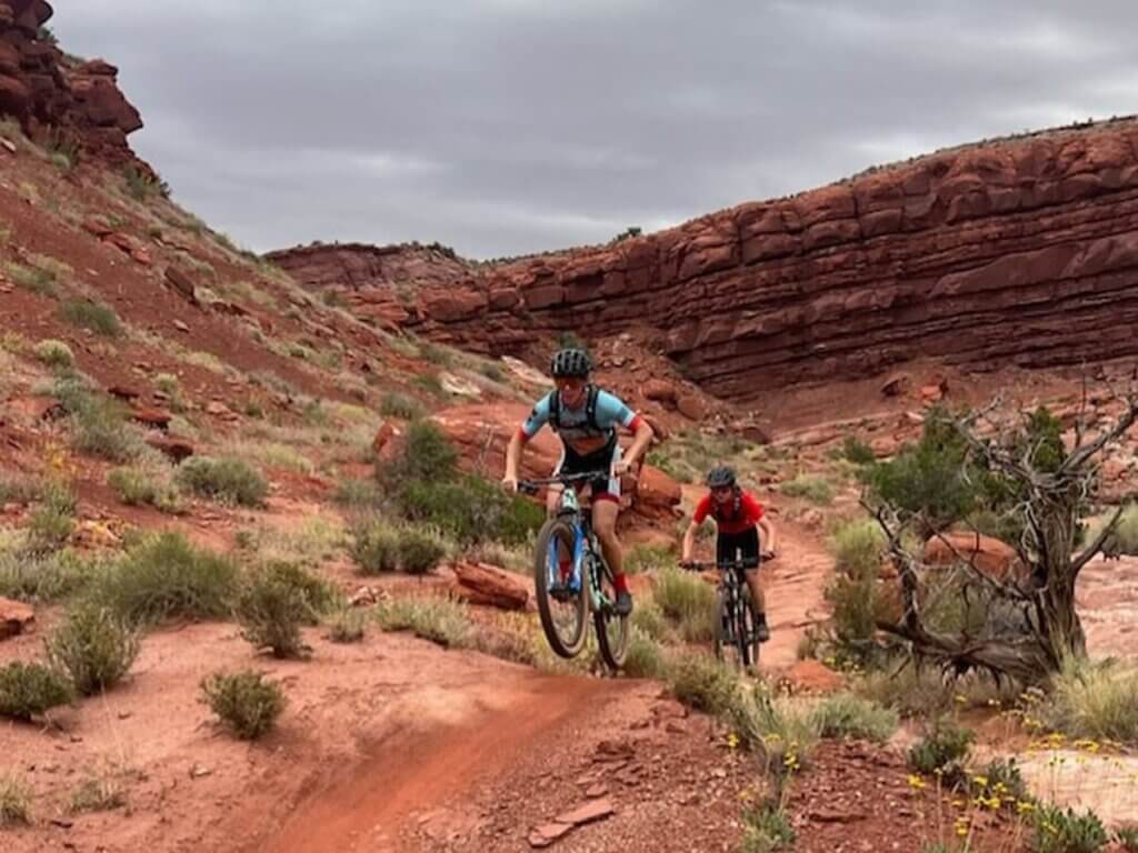 bikers travel across mountainous desert terrain near moab utah