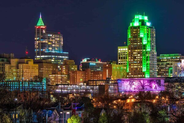 a nighttime view of the downtown raleigh, north carolina skyline with buildings lit up in neon lights of green and pink