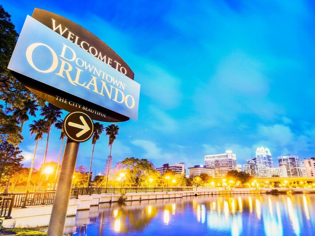 "Welcome To Downtown Orlando" sign with bay, boats, and lights in the background