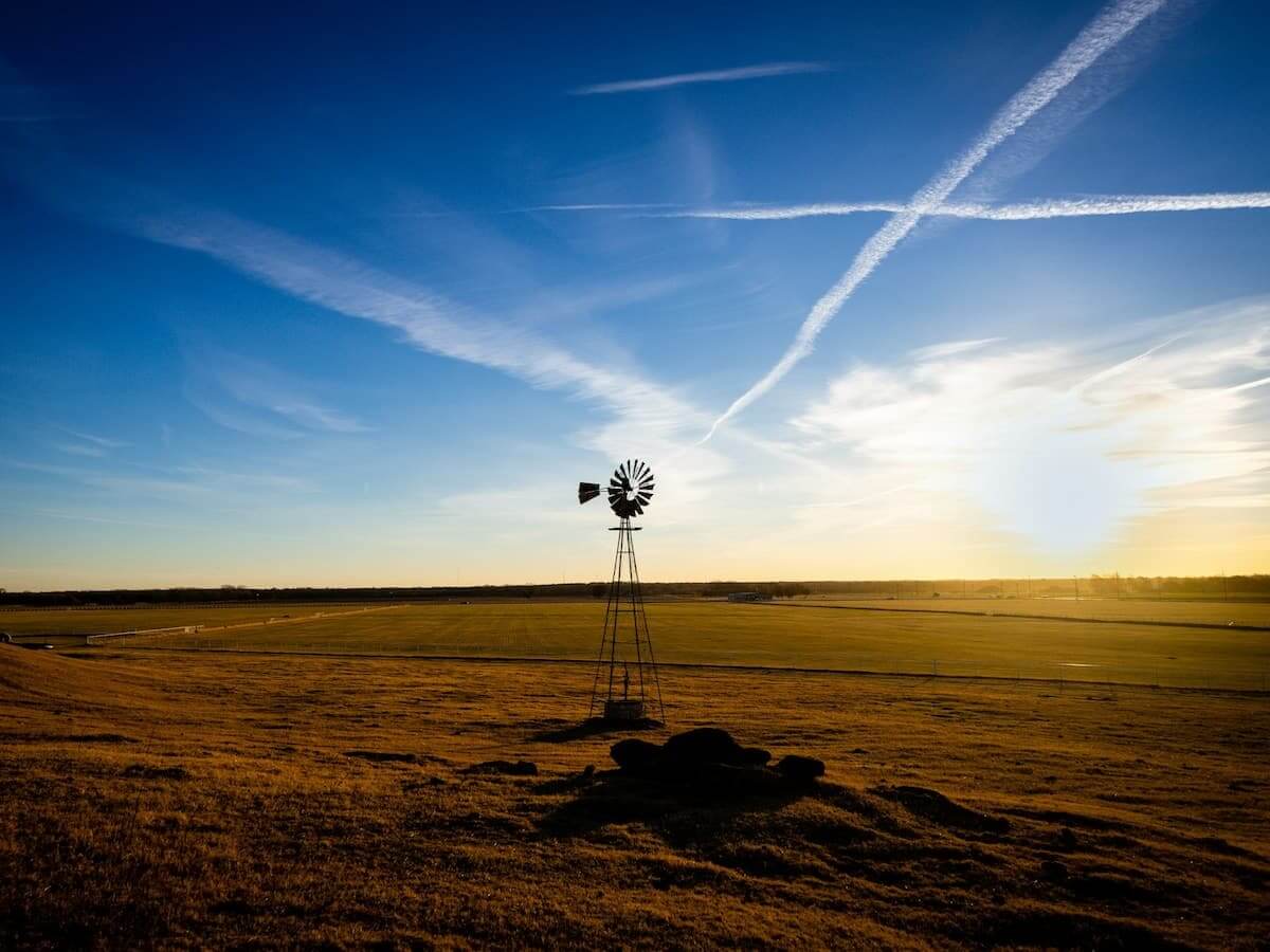 the sun sets behind a windmill in an open oklahoma field