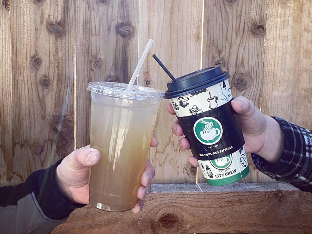 Two people tilting their drinks together from City Brew Coffee